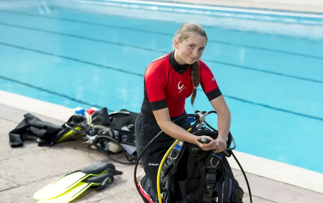 Student in diving gear smiling next to pool