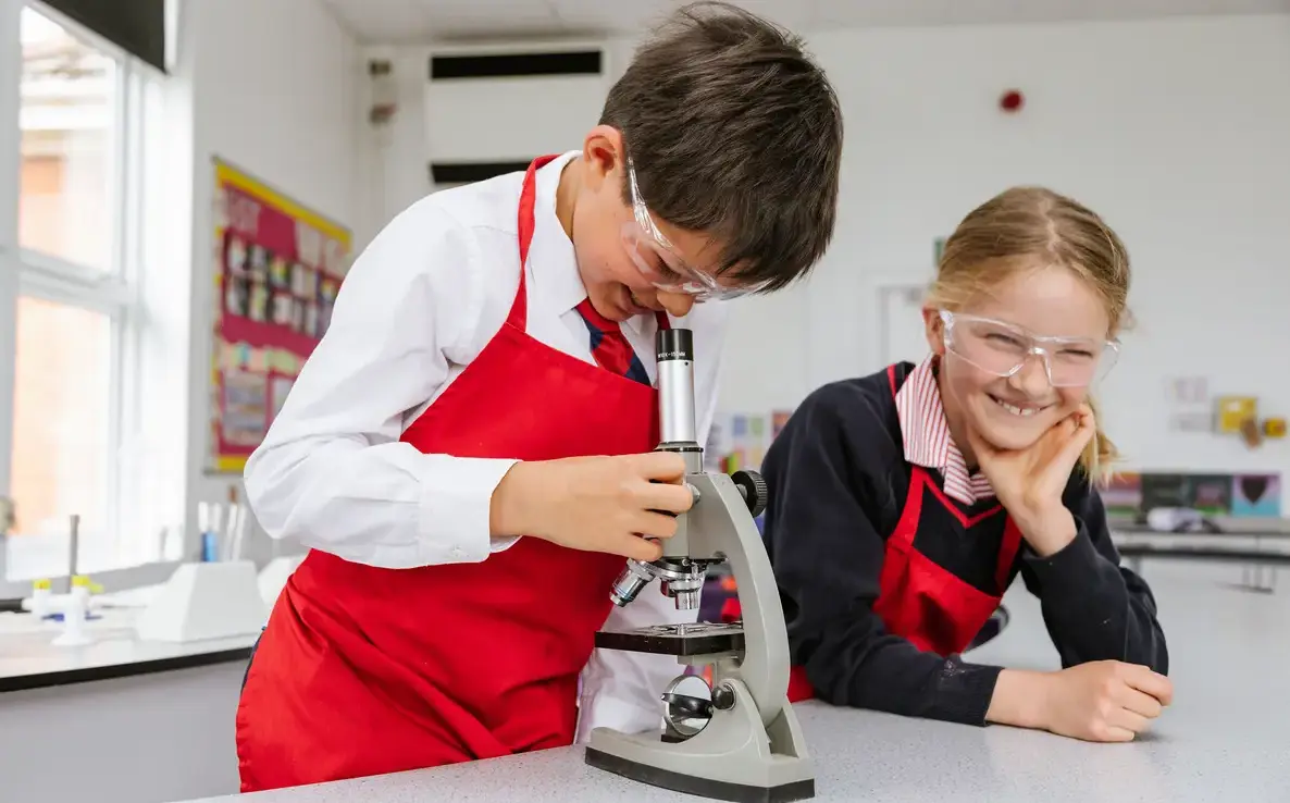 boy looking in to microscope and girl watching him smiling in prep school science lab blundells pre school private prep school in devon