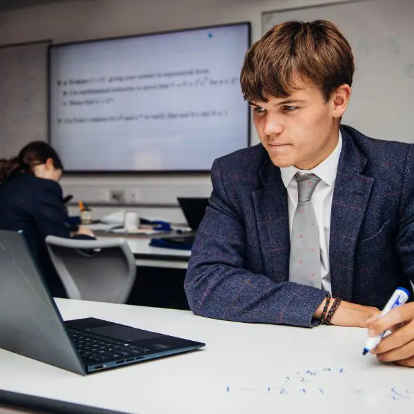 Pupil looking at laptop drawing maths workings out on whiteboard table private education devon